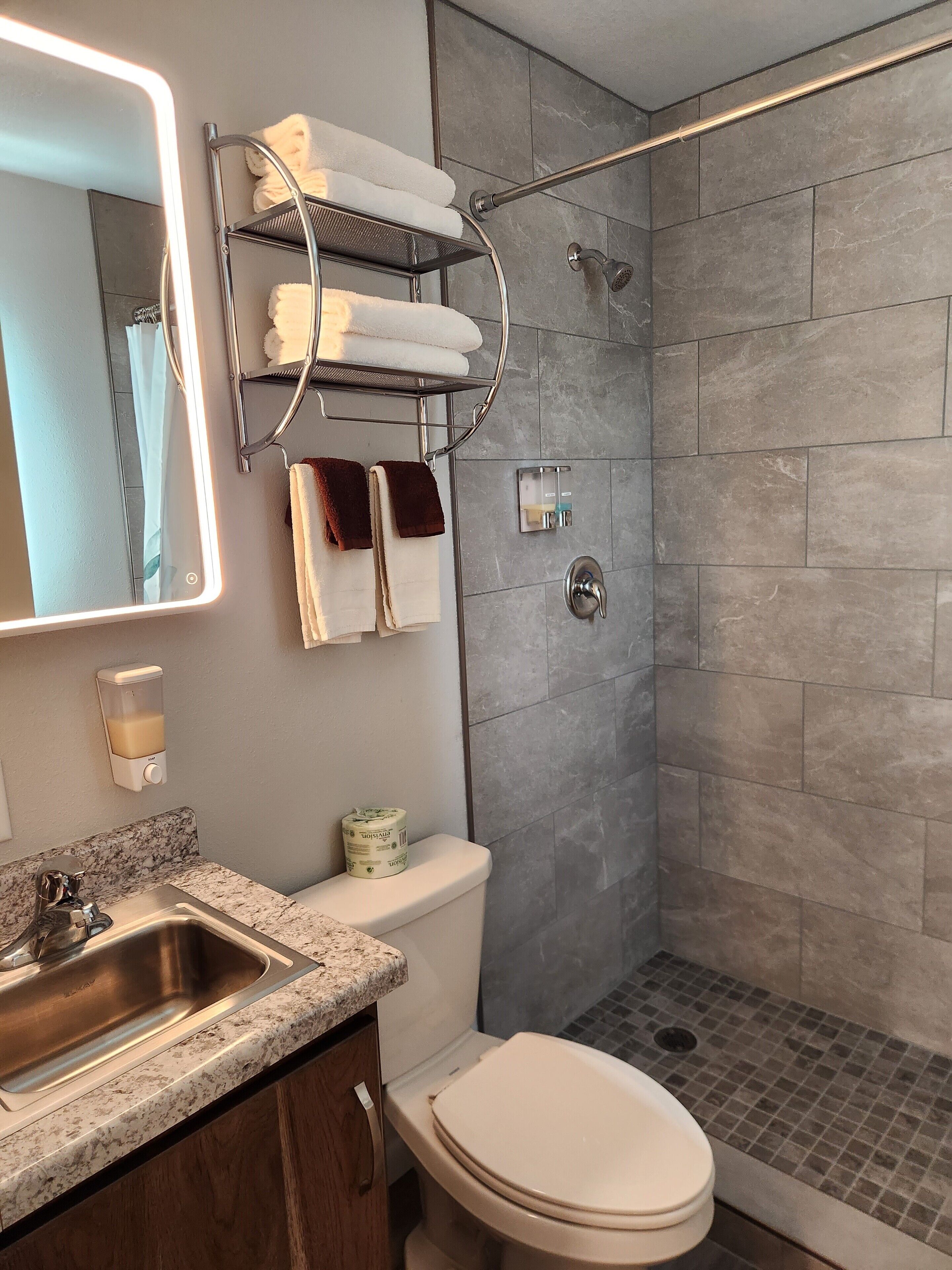 Ein modernes Badezimmer mit Dusche, Toilette, Waschbecken und einem Handtuchhalter mit mehreren Handtüchern.