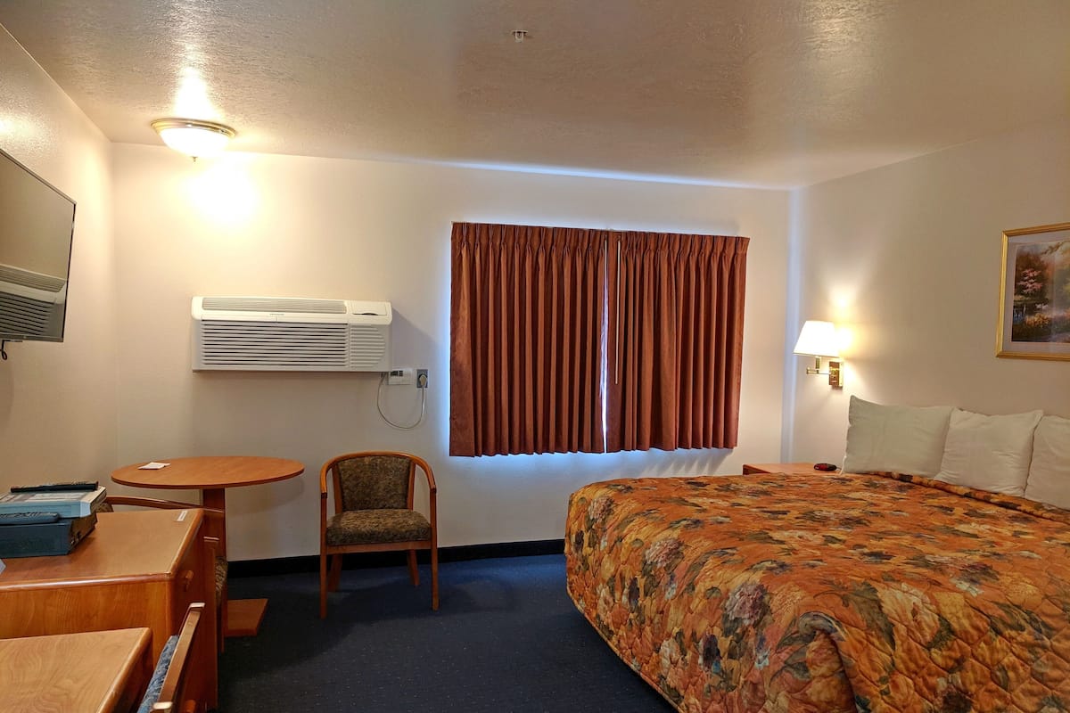 Ein Hotelzimmer mit Bett, Schreibtisch, Stuhl, Klimaanlage, einem Fenster mit Vorhängen und einer Wandlampe.