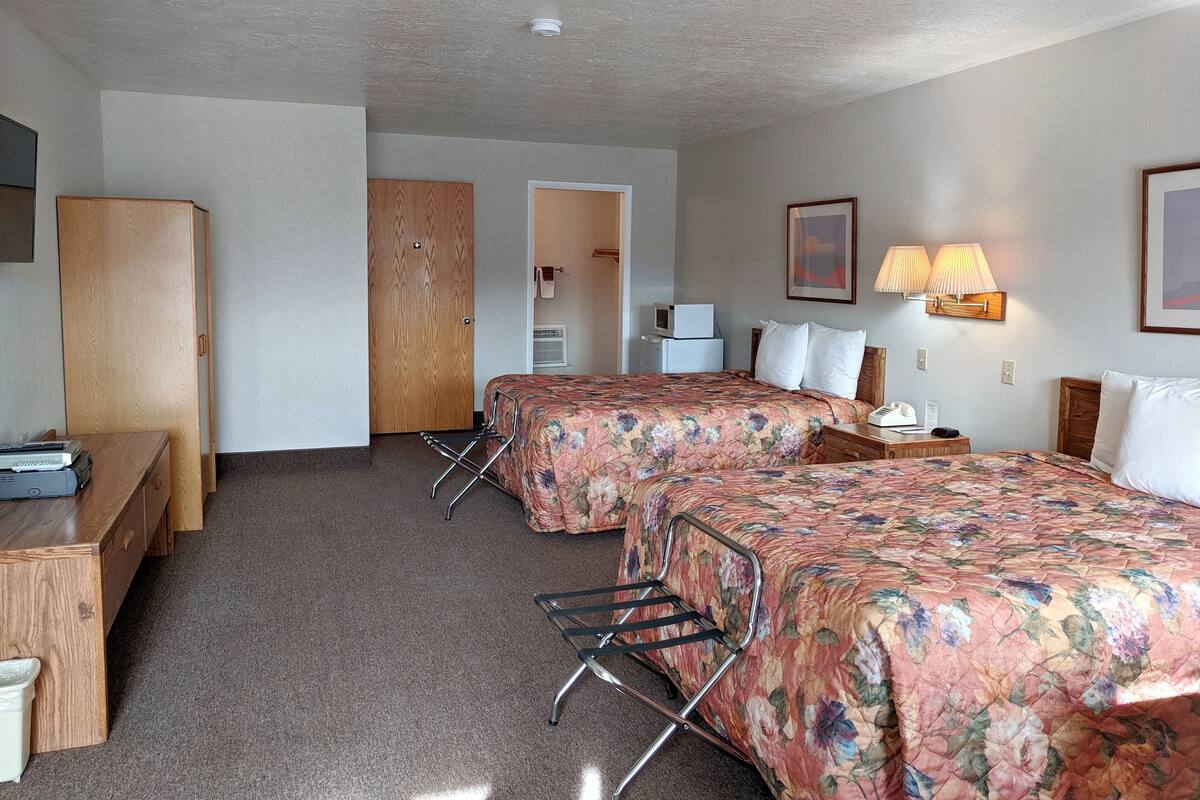 Ein Hotelzimmer mit zwei Betten, einem Schreibtisch, einem Kleiderschrank und einer Lampe.