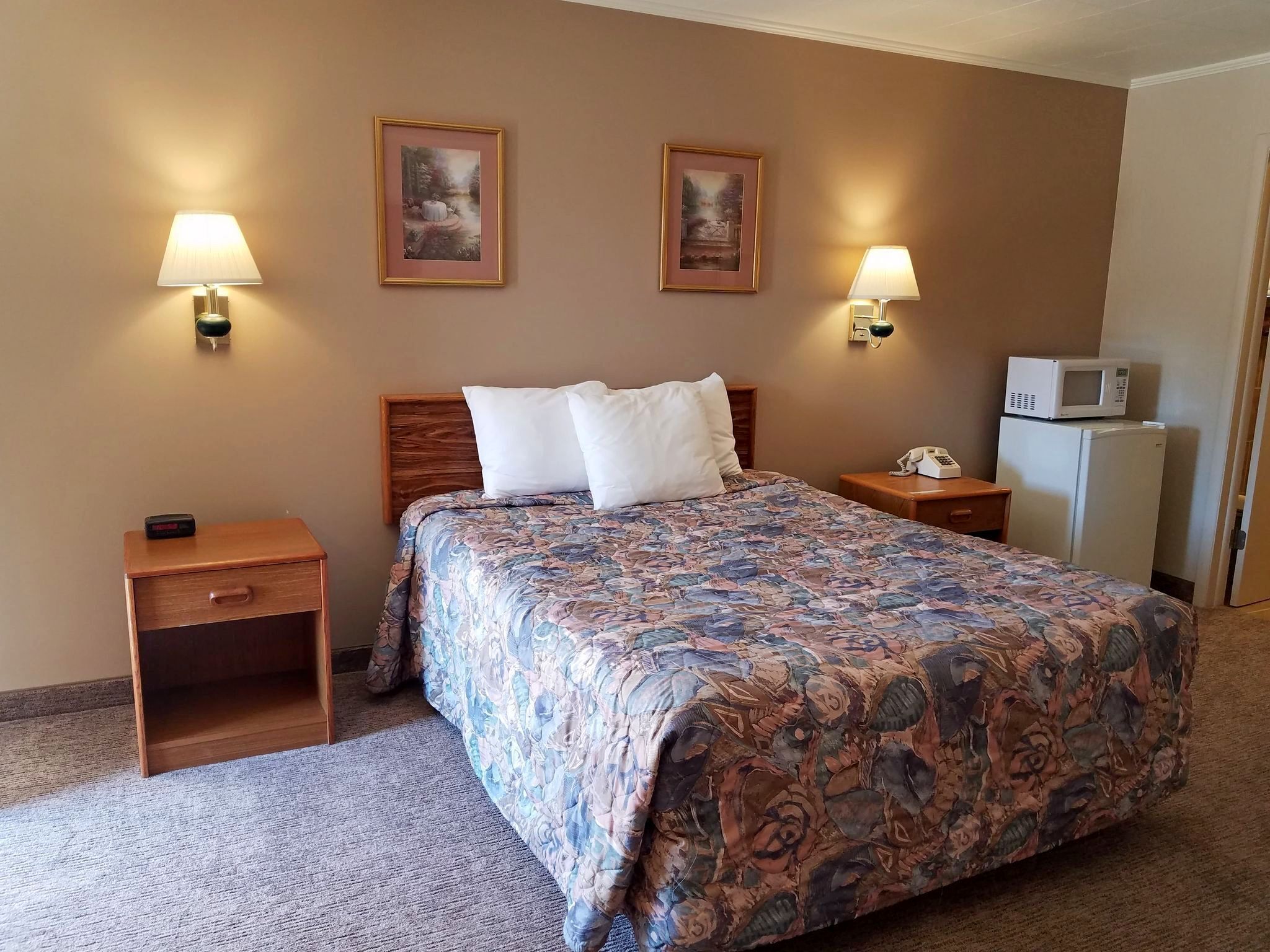 Une chambre d’hôtel avec un grand lit, deux lampes fixées au mur, une table de chevet avec un téléphone, un four à micro-ondes et un réfrigérateur.