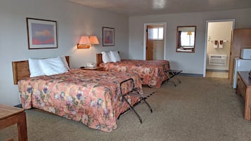 A hotel room with two beds, a desk, a chair, a lamp, and a door leading to another room.