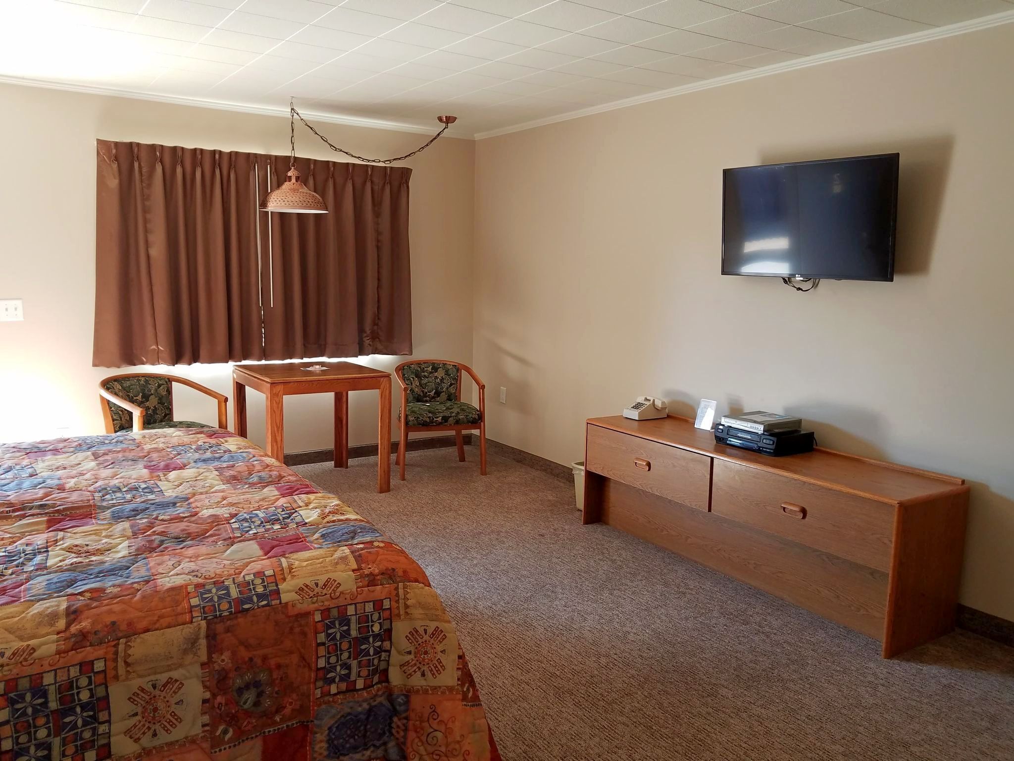 A hotel room with a bed, a desk, a chair, a television, and a dresser.