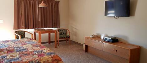 A hotel room with a bed, a desk, a chair, a television, and a dresser.