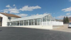 Un edificio bajo y alargado con una estructura de vidrio, posiblemente un invernadero o salón de plantas, adyacente a un edificio blanco con techo marrón.
