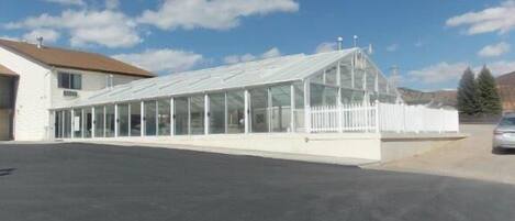 A long, single-story building with a glass-enclosed structure, likely a greenhouse or conservatory, adjacent to a white building with a brown roof.