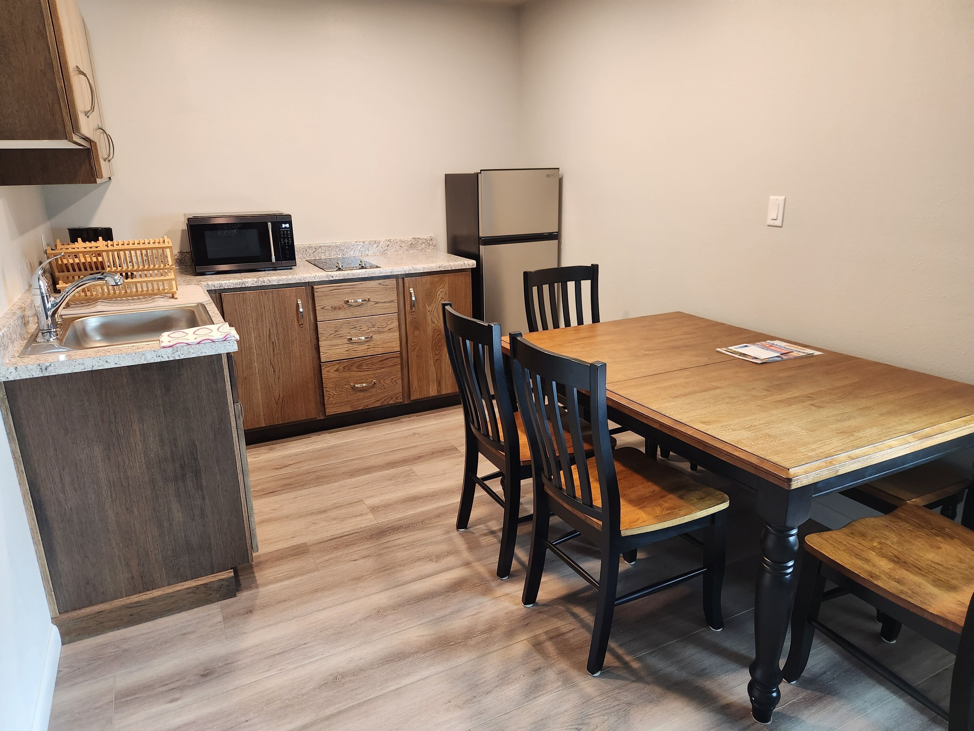 A compact kitchen with a wooden table and chairs, a microwave, a refrigerator, and a sink.