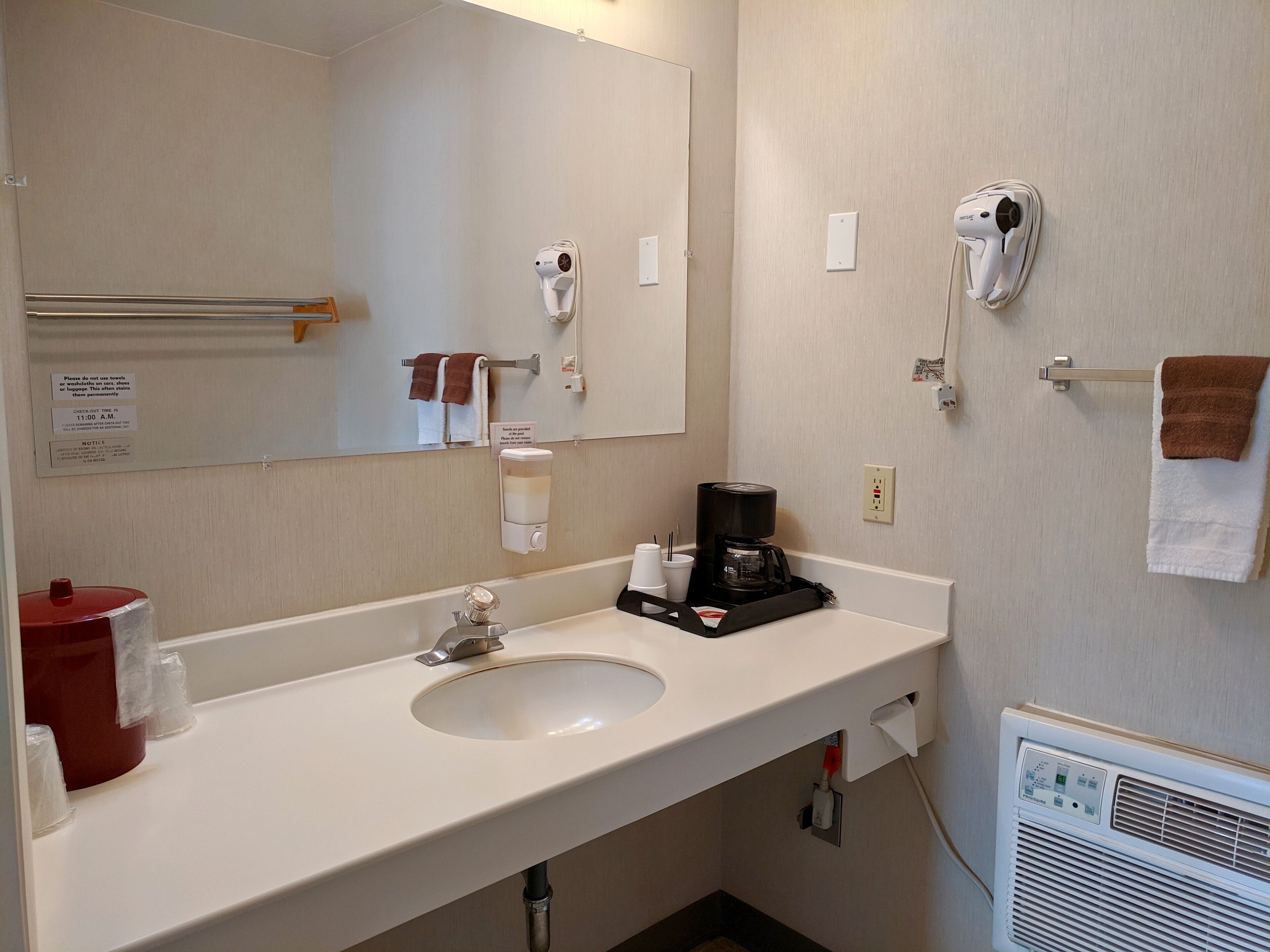 Baño de hotel con lavamanos, espejo, toallero, secador de pelo y cafetera.