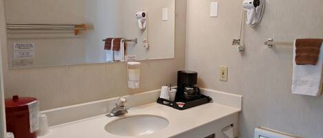 Baño de hotel con lavamanos, espejo, toallero, secador de pelo y cafetera.
