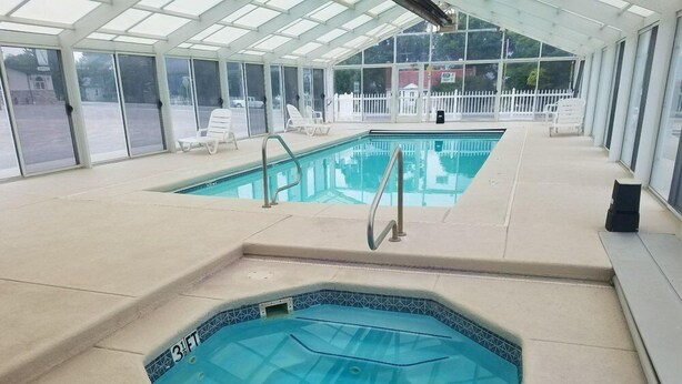 Una piscina techada con un jacuzzi, sillas de descanso y una cerca blanca al fondo.