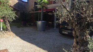 A gravel driveway leading to a parked car, a palm tree, and a building with a red awning. - The Resid For Calixte (Perouges)