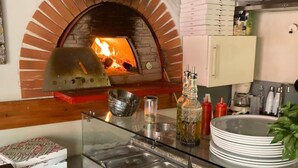 A kitchen with a brick oven, a glass counter with plates, and a stack of pizza boxes. - The Resid For Calixte (Perouges)