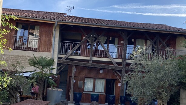 A rustic building with a wooden balcony, a gravel courtyard, and outdoor seating. - The Resid For Calixte (Perouges)