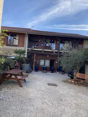 A rustic building with a wooden balcony, a gravel courtyard, and outdoor seating.
