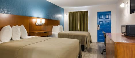 A hotel room with two beds, a wooden headboard, a desk with a television, and a blue door.