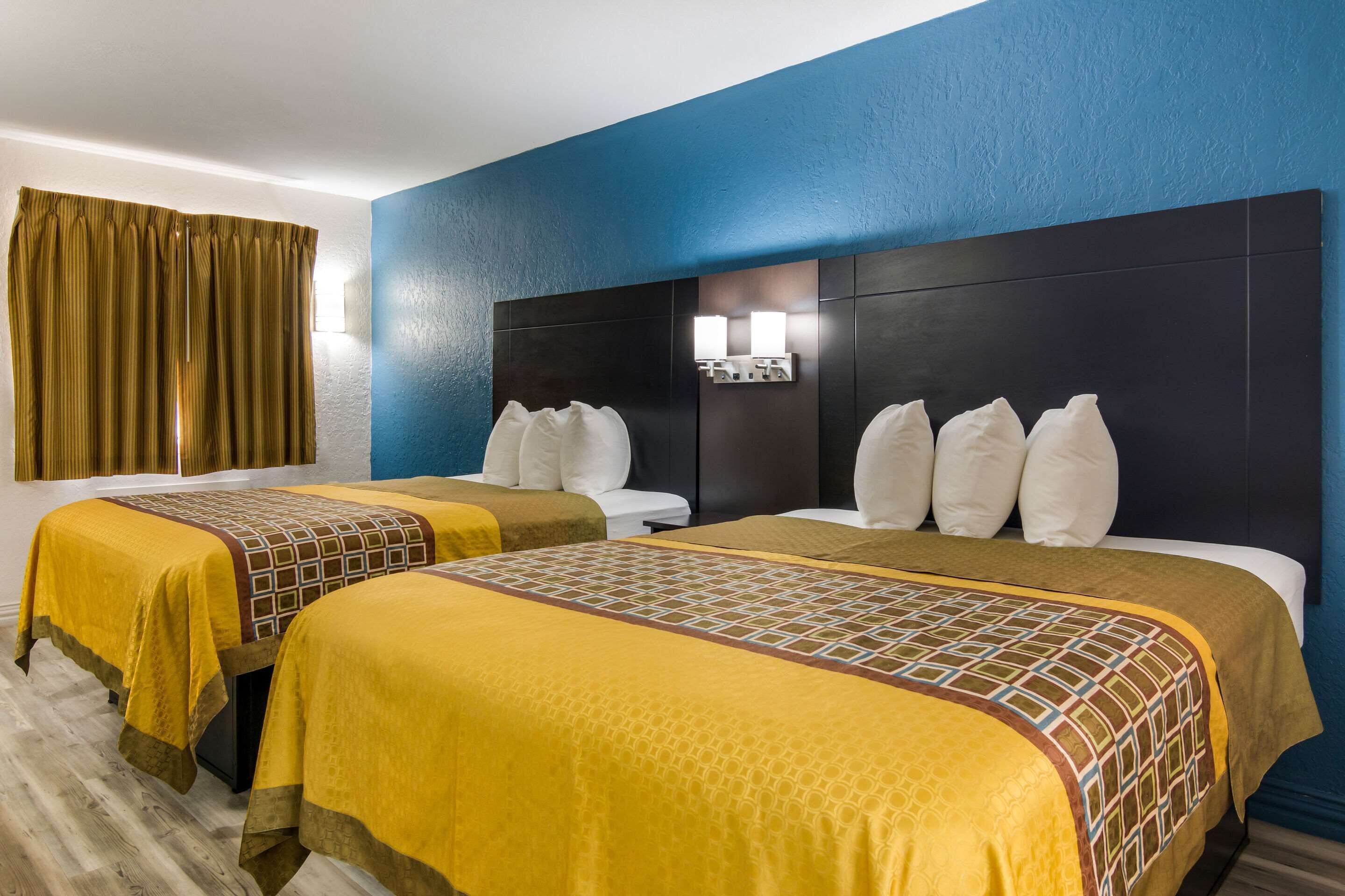 A hotel room with two beds, a large headboard, and a bathroom with a white toilet.