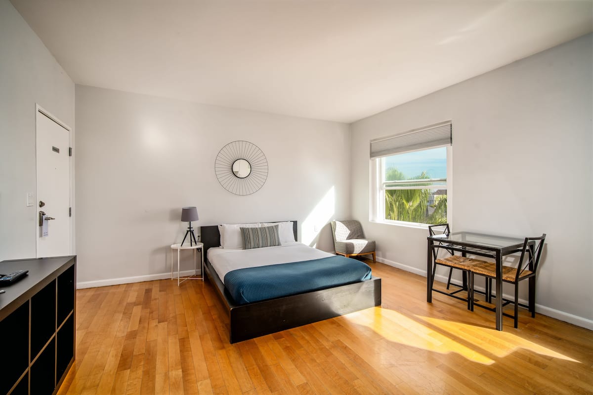 Ein modernes Schlafzimmer mit Bett, Nachttisch, Lampe, Stuhl und Blick ins Freie.