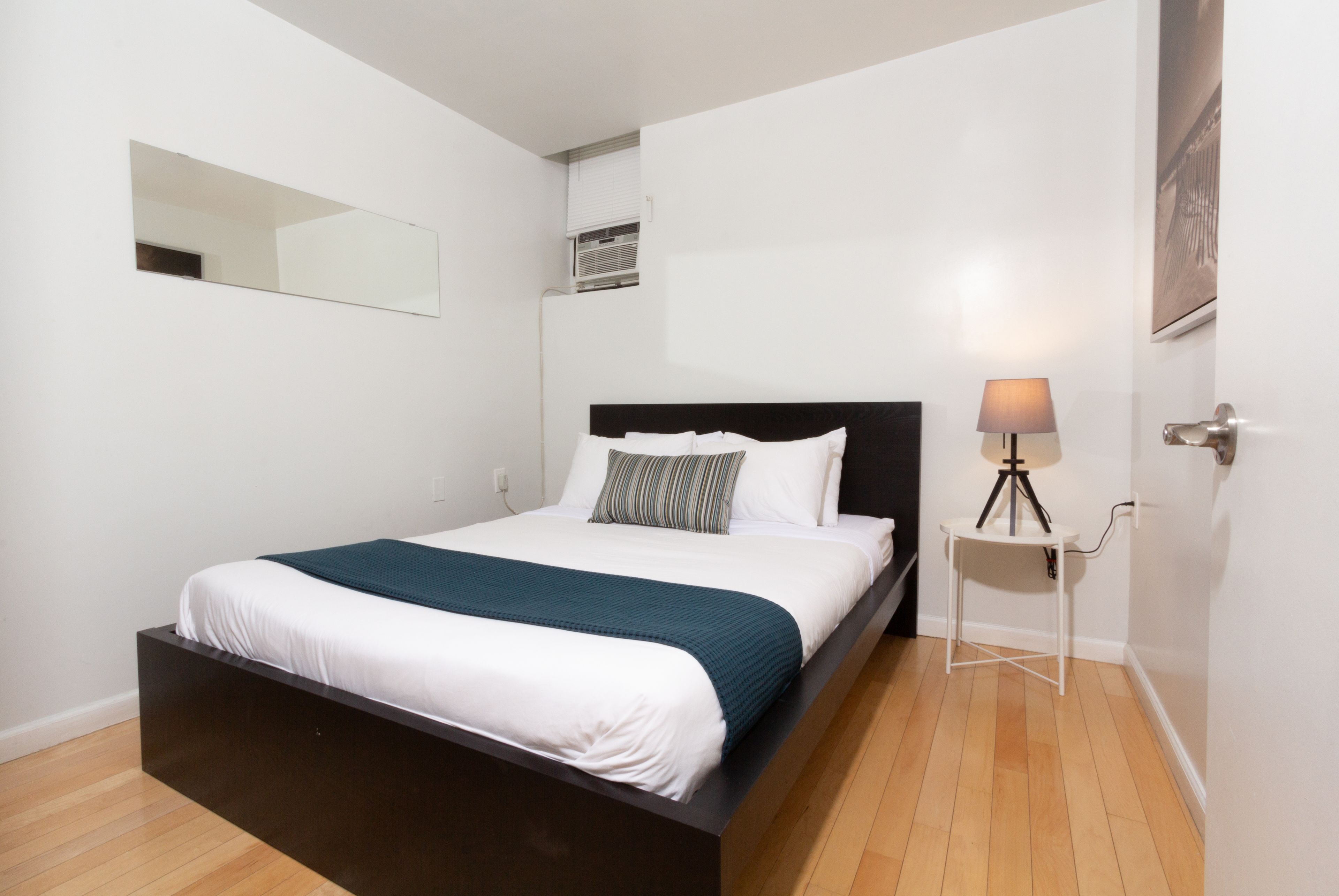 A modern bedroom with a bed, a bedside table with a lamp, and a wall-mounted mirror.