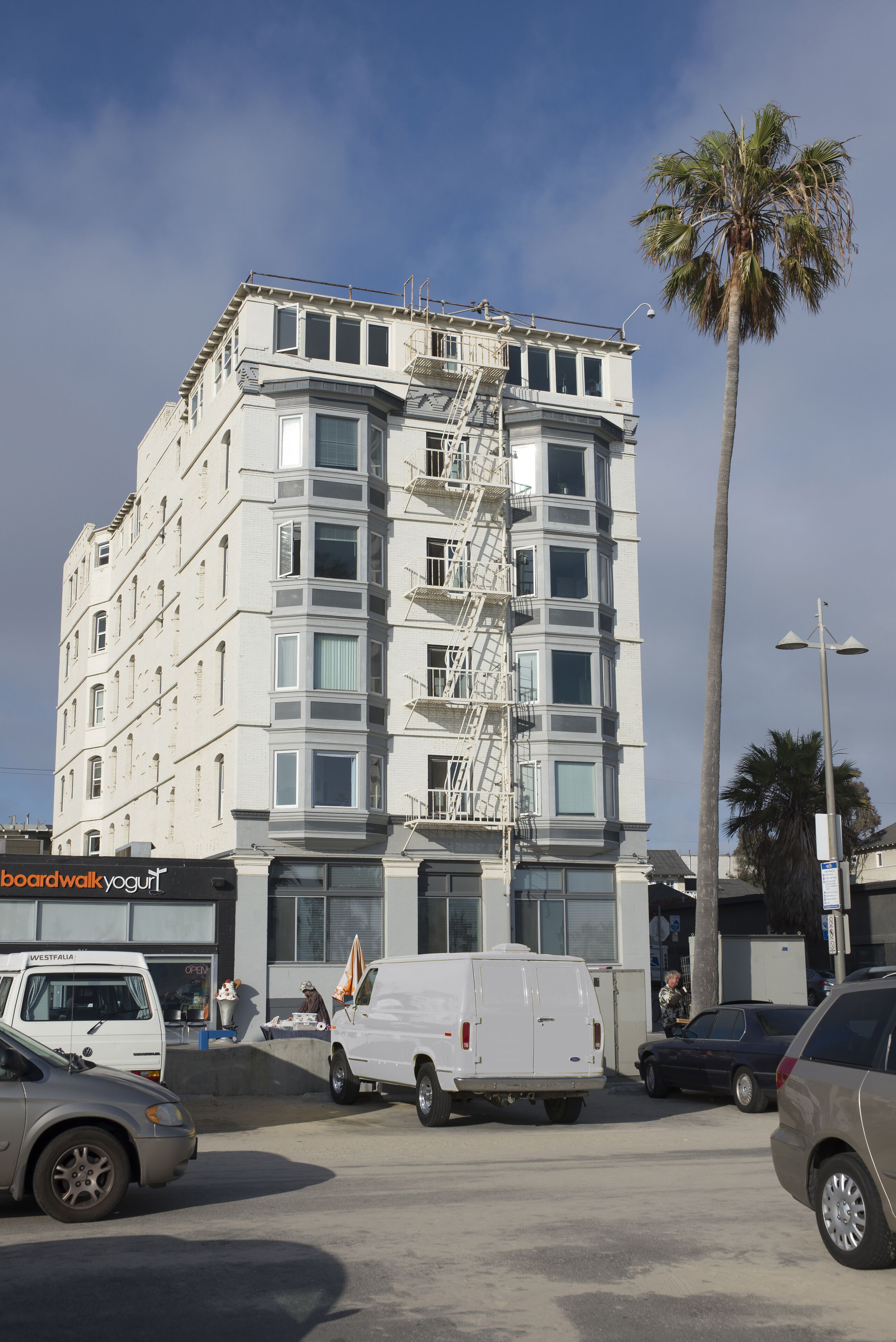 A multi-story building with a fire escape, parked vehicles, and a palm tree.