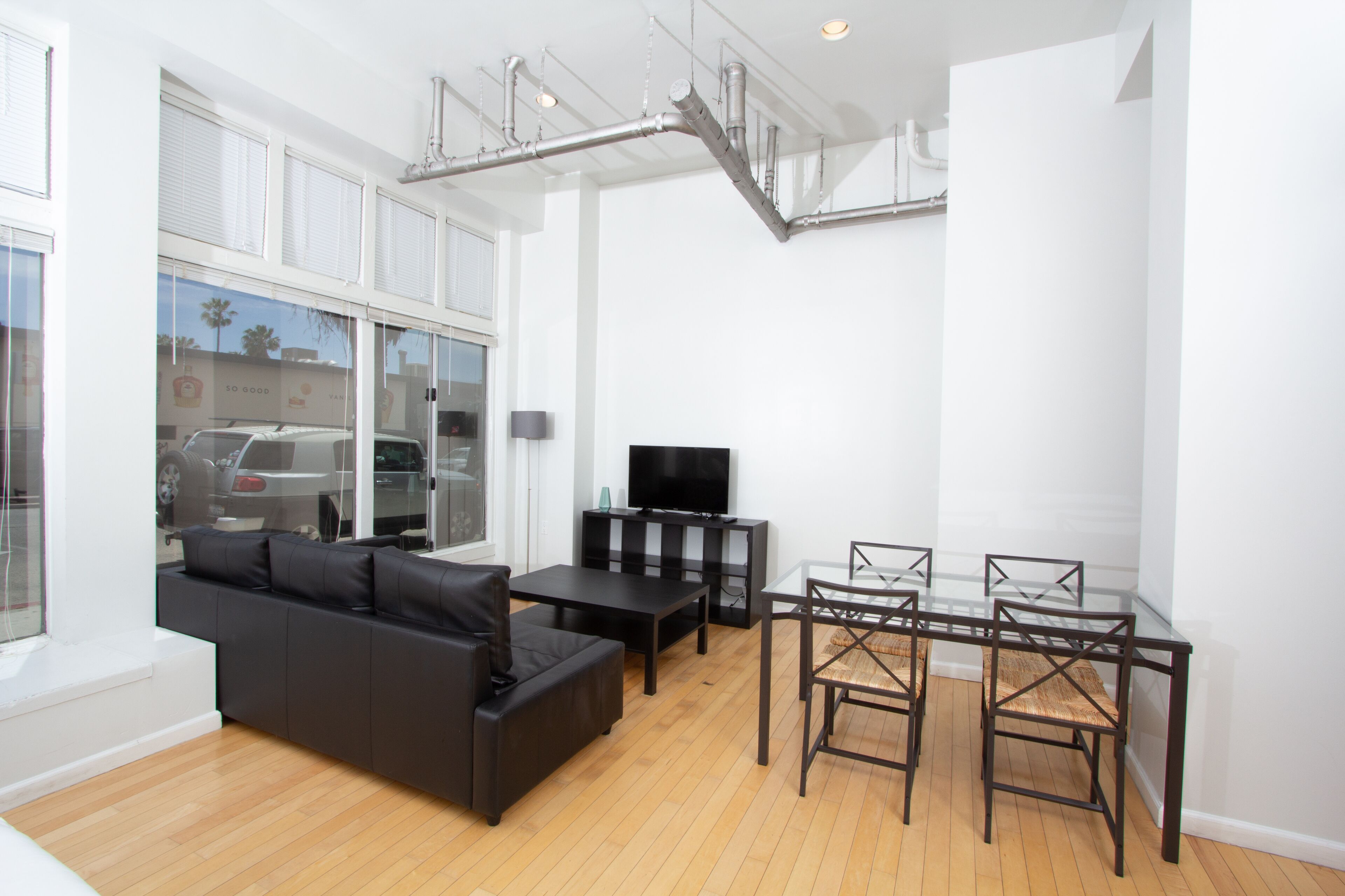 A modern living room with a black sofa, a glass dining table, and a TV.