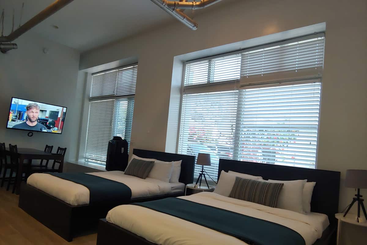 Ein Hotelzimmer mit zwei Betten, einem Fernseher, einem Schreibtisch und großen Fenstern.