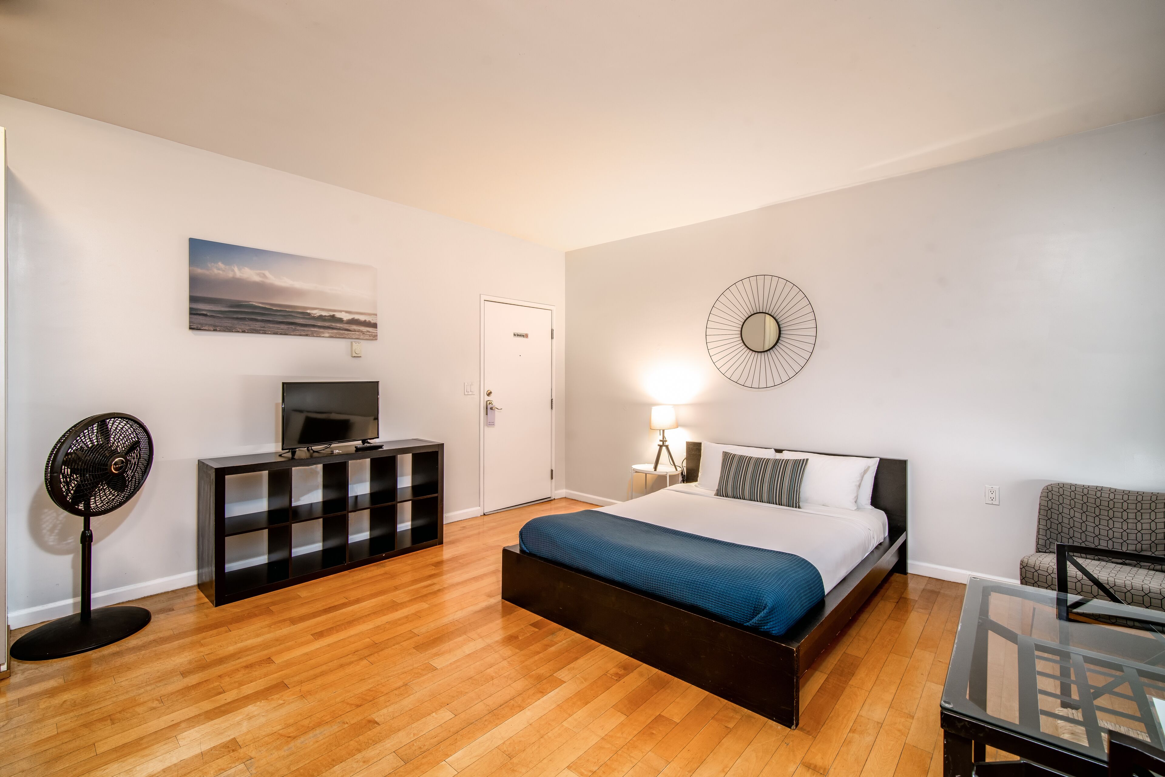 A modern bedroom with a bed, a TV, a fan, a dresser, and a wall-mounted clock.