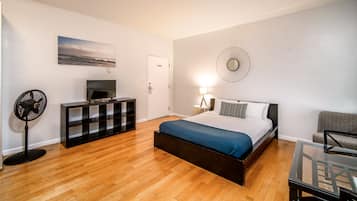A modern bedroom with a bed, a TV, a fan, a dresser, and a wall-mounted clock.