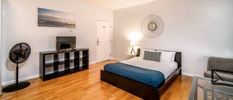 A modern bedroom with a bed, a TV, a fan, a dresser, and a wall-mounted clock.