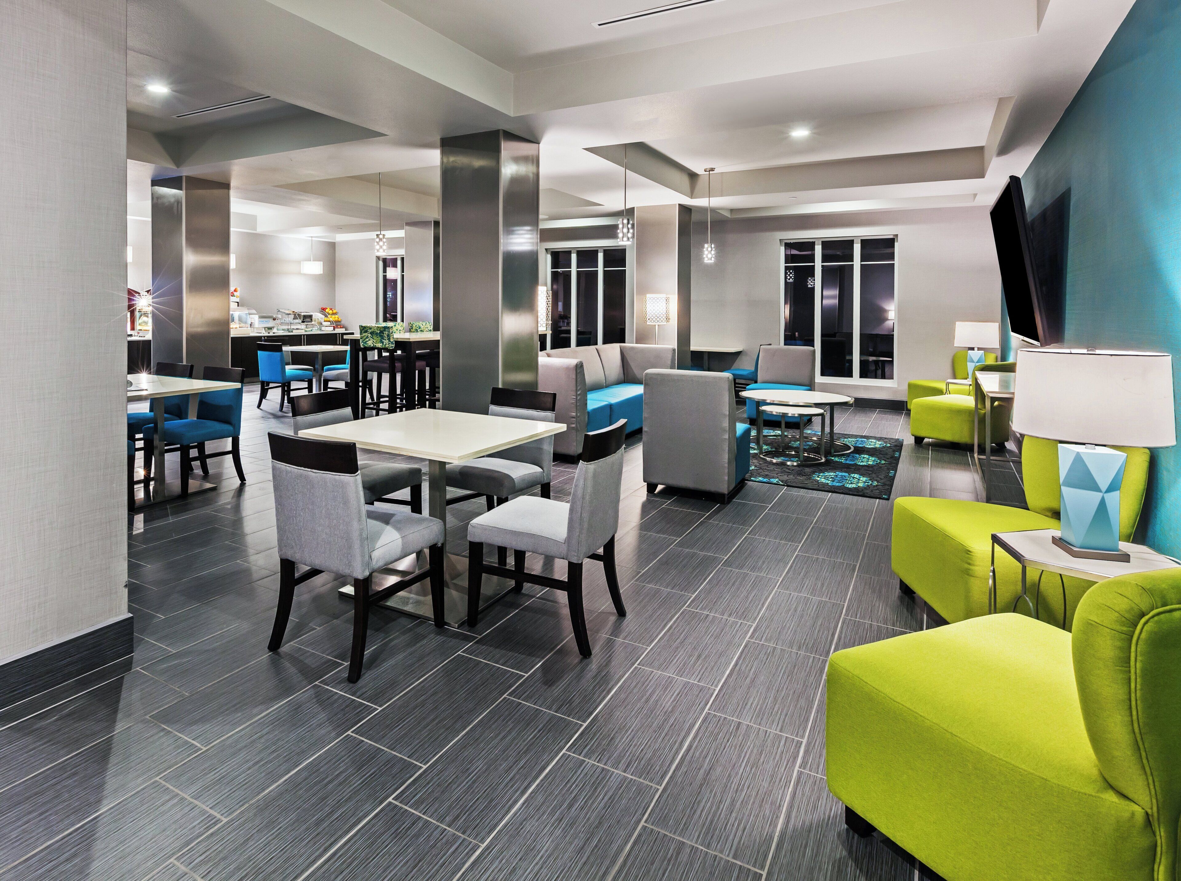 A modern hotel lobby with a dining area, seating arrangements, and a television screen.