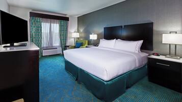 Habitación de hotel con cama, mesitas de noche, escritorio con televisor de pantalla plana, ventana con cortinas y alfombra estampada.
