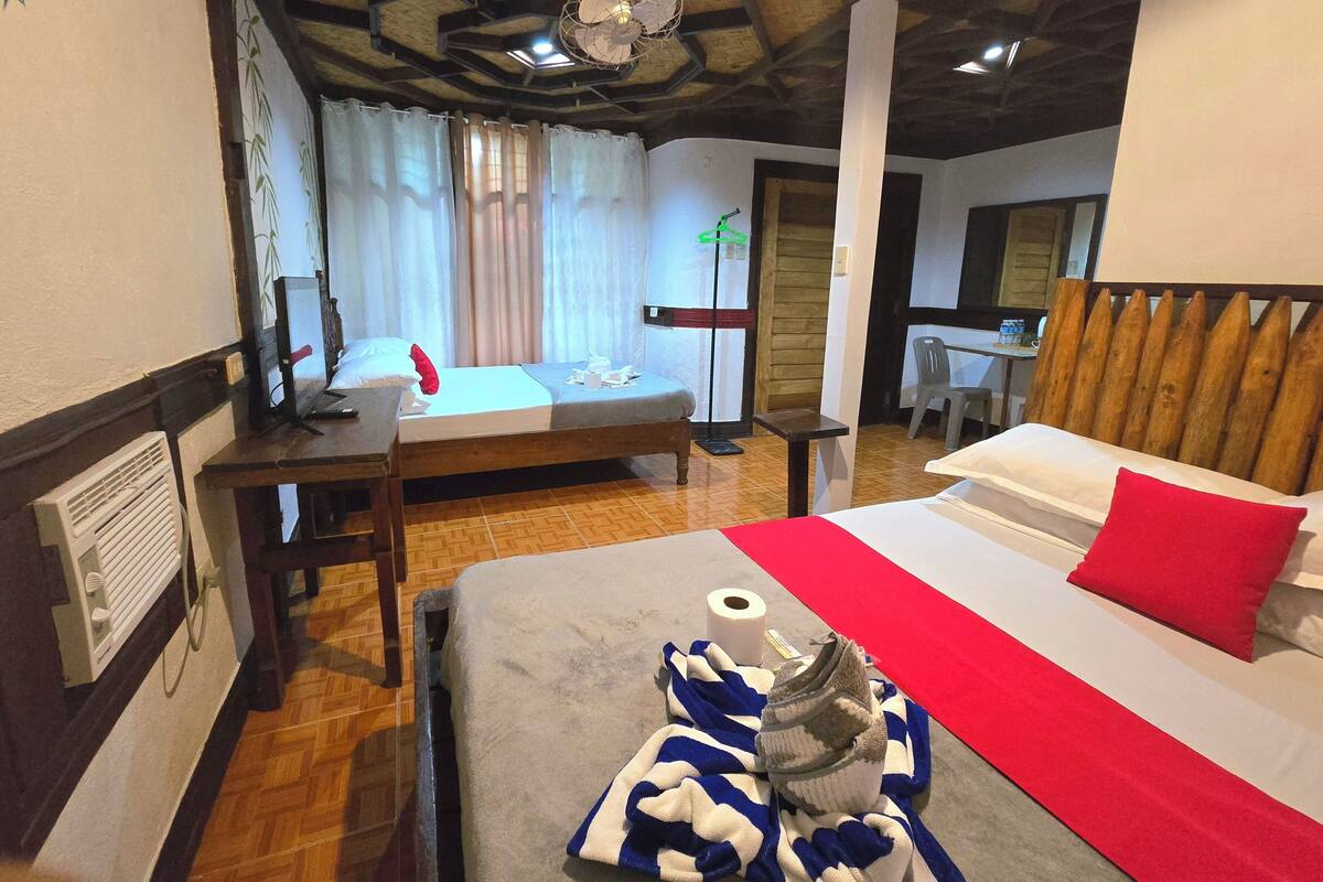 Habitación de hotel con cama, escritorio, silla, calefactor y ventana con cortinas.