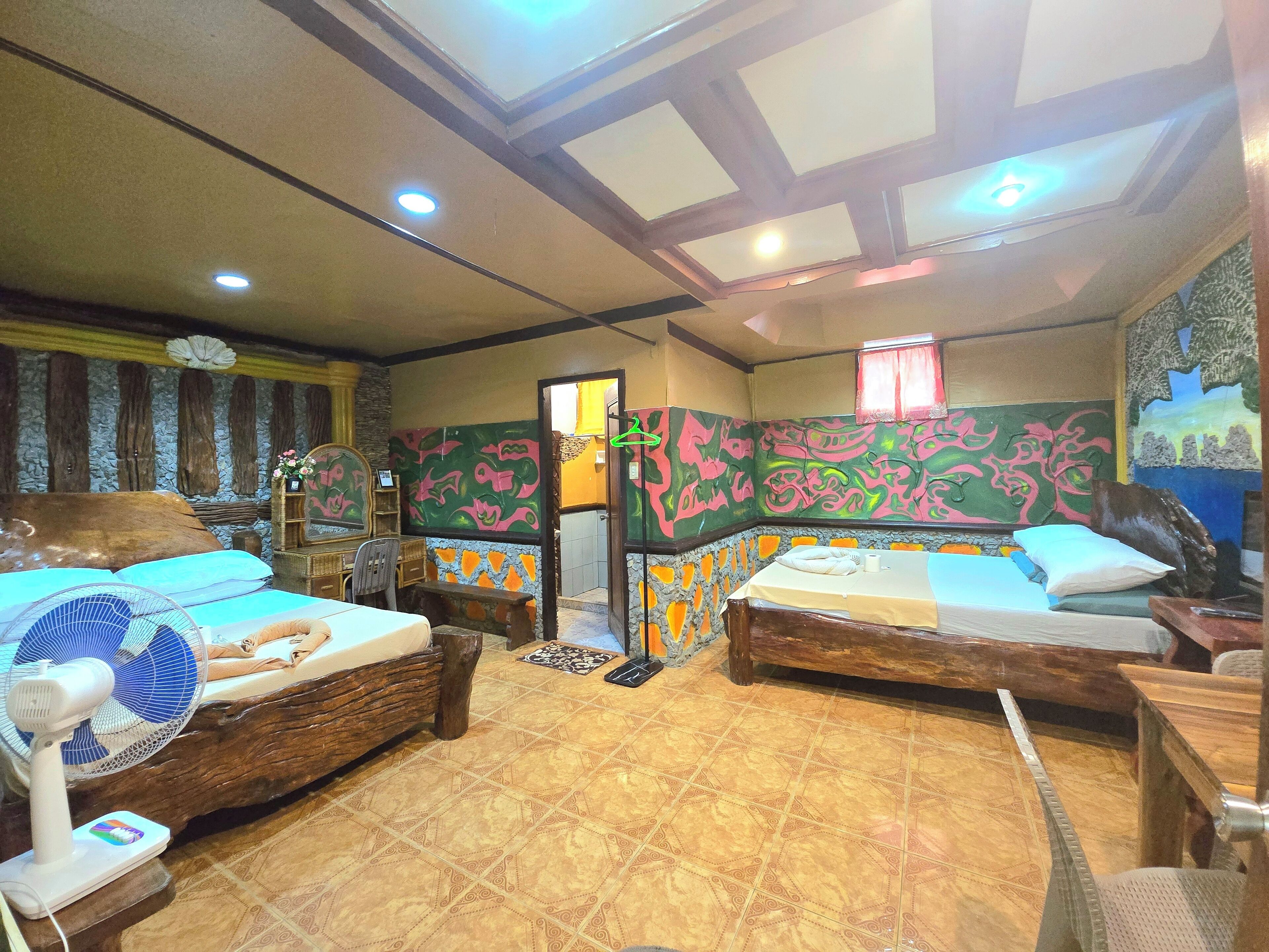 A room with two beds, a fan, a mirror, and a decorative wall.