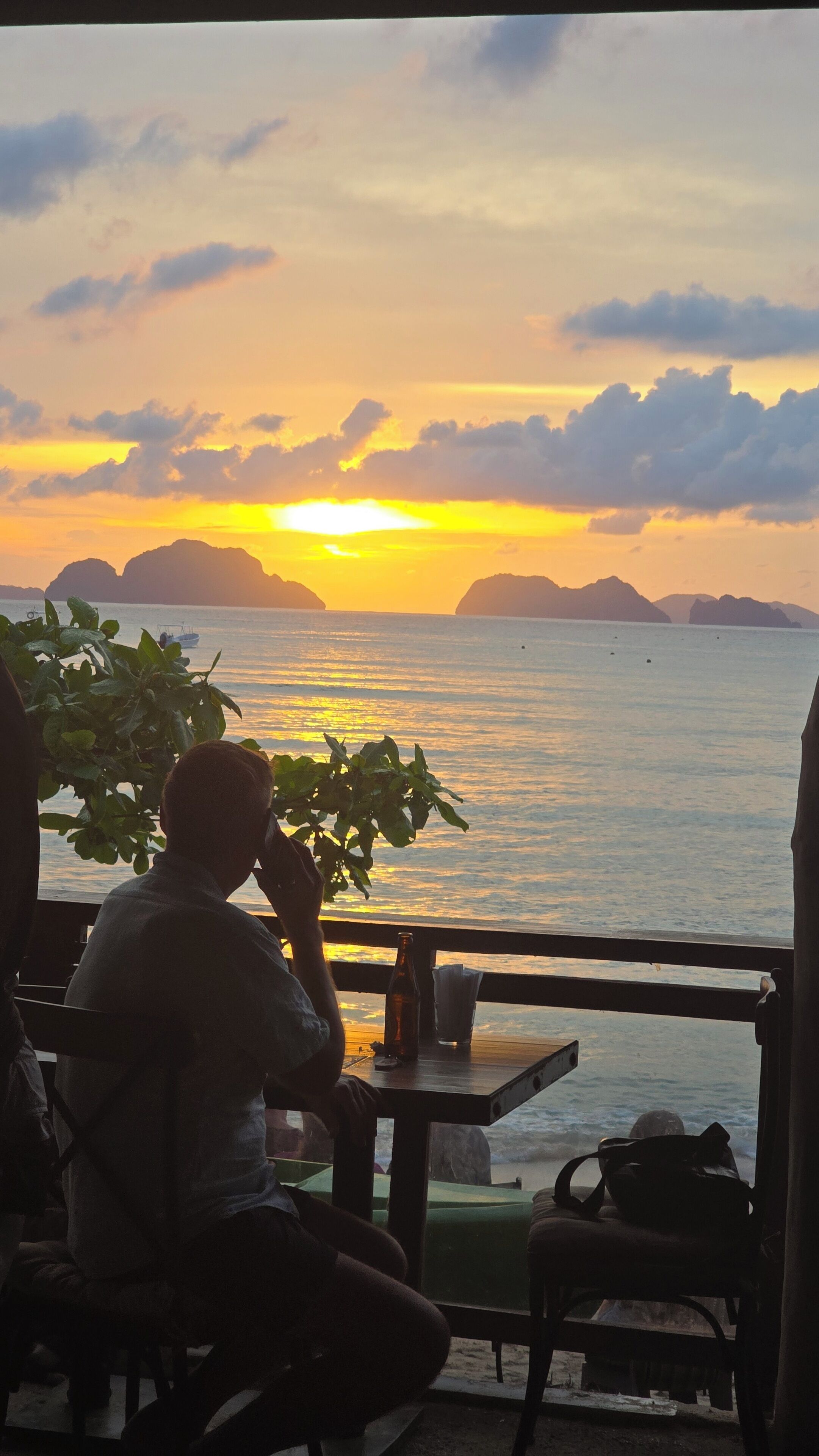 A person sitting at a table with a view of the sunset over the water.