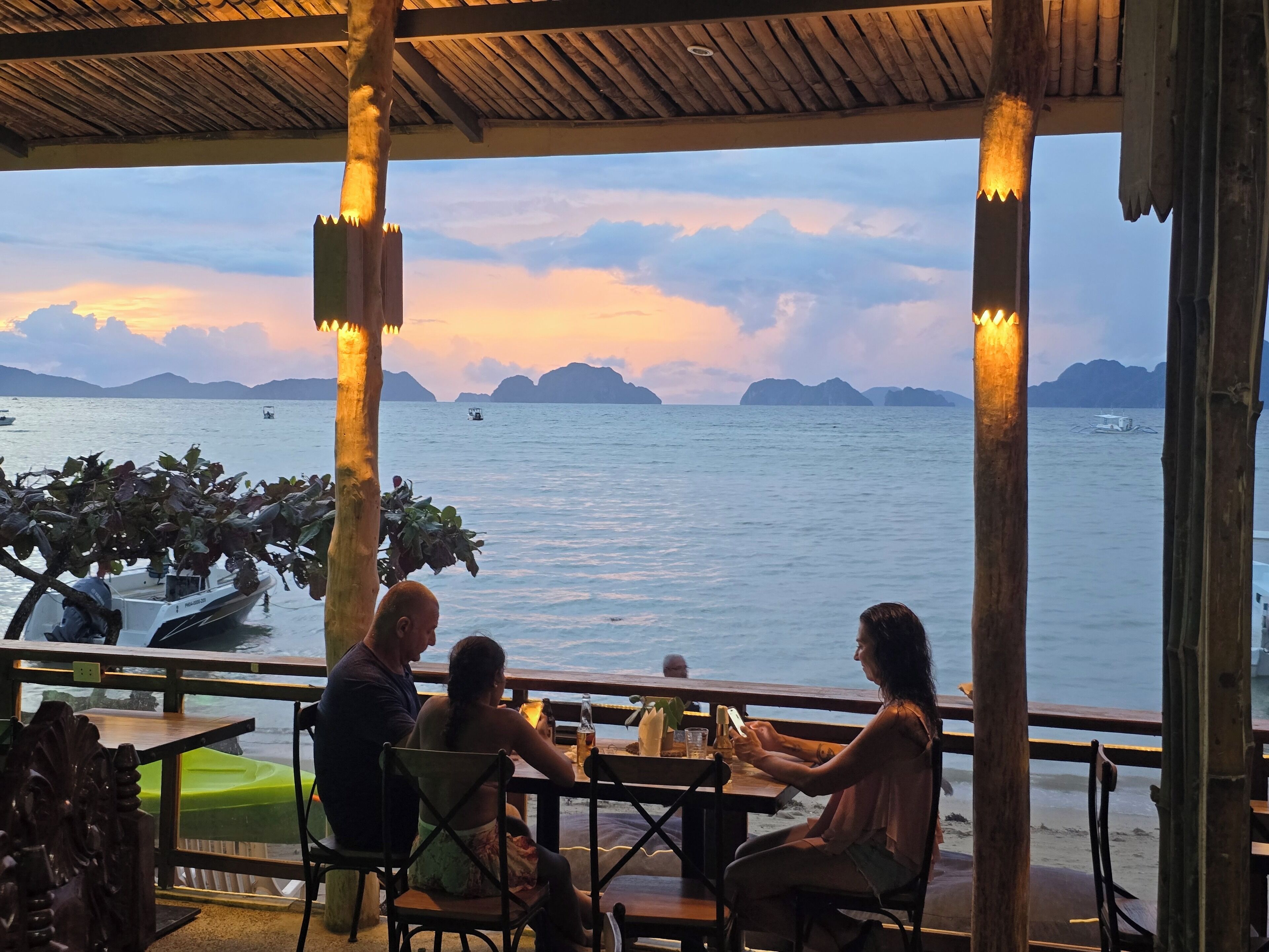A restaurant with a view of the sea and mountains. There are tables and chairs for dining.