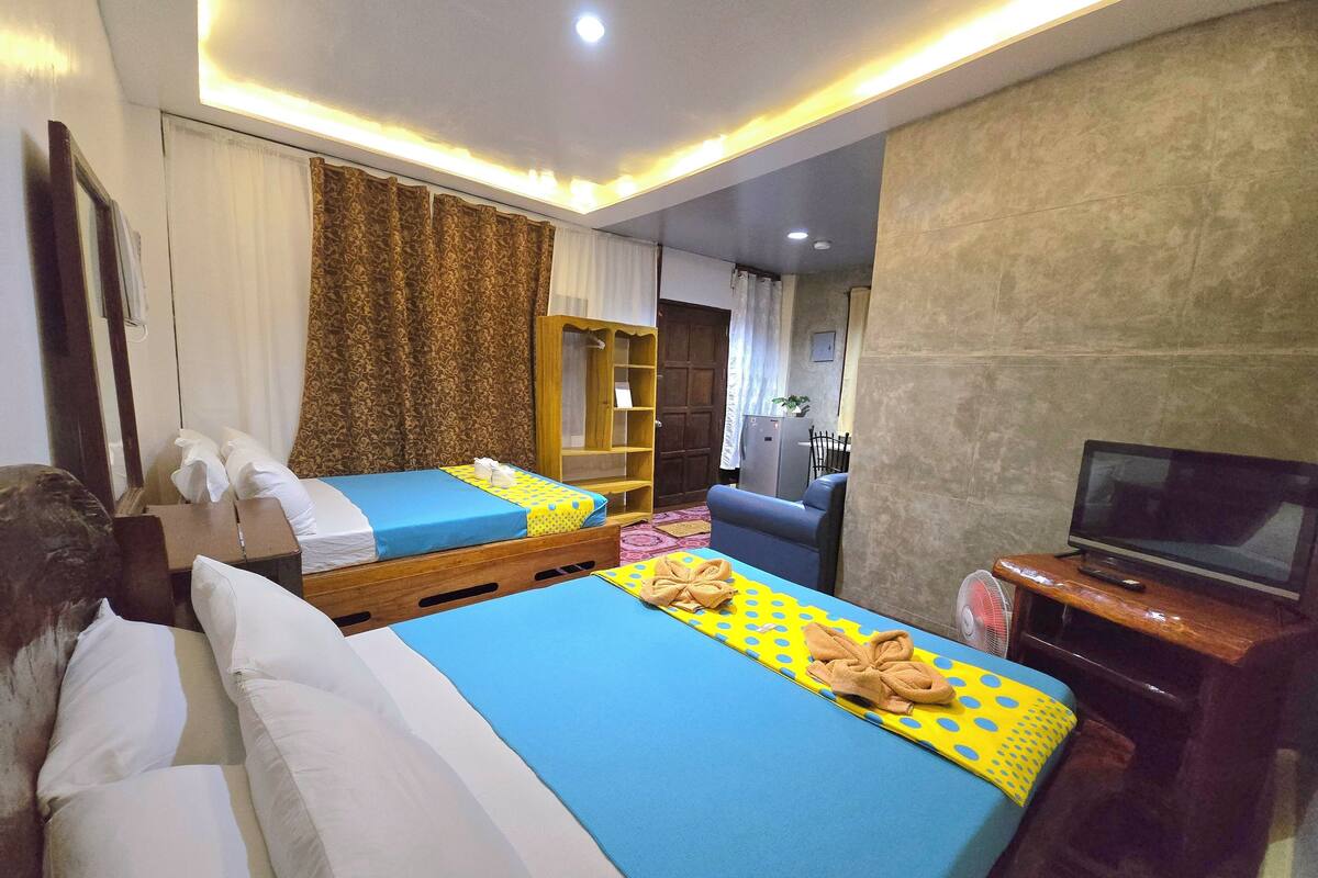 Habitación de hotel con dos camas, un televisor y un escritorio pequeño.