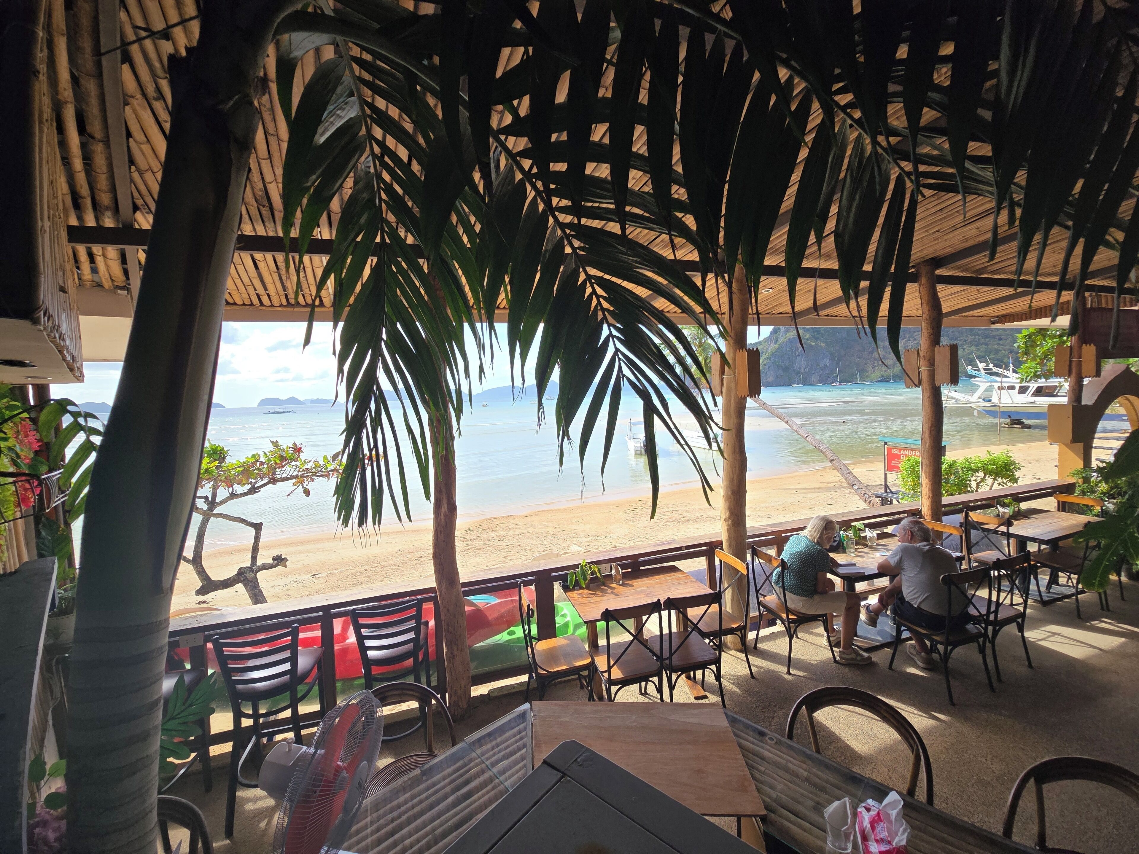 An outdoor seating area with tables and chairs, overlooking a beach and the sea.
