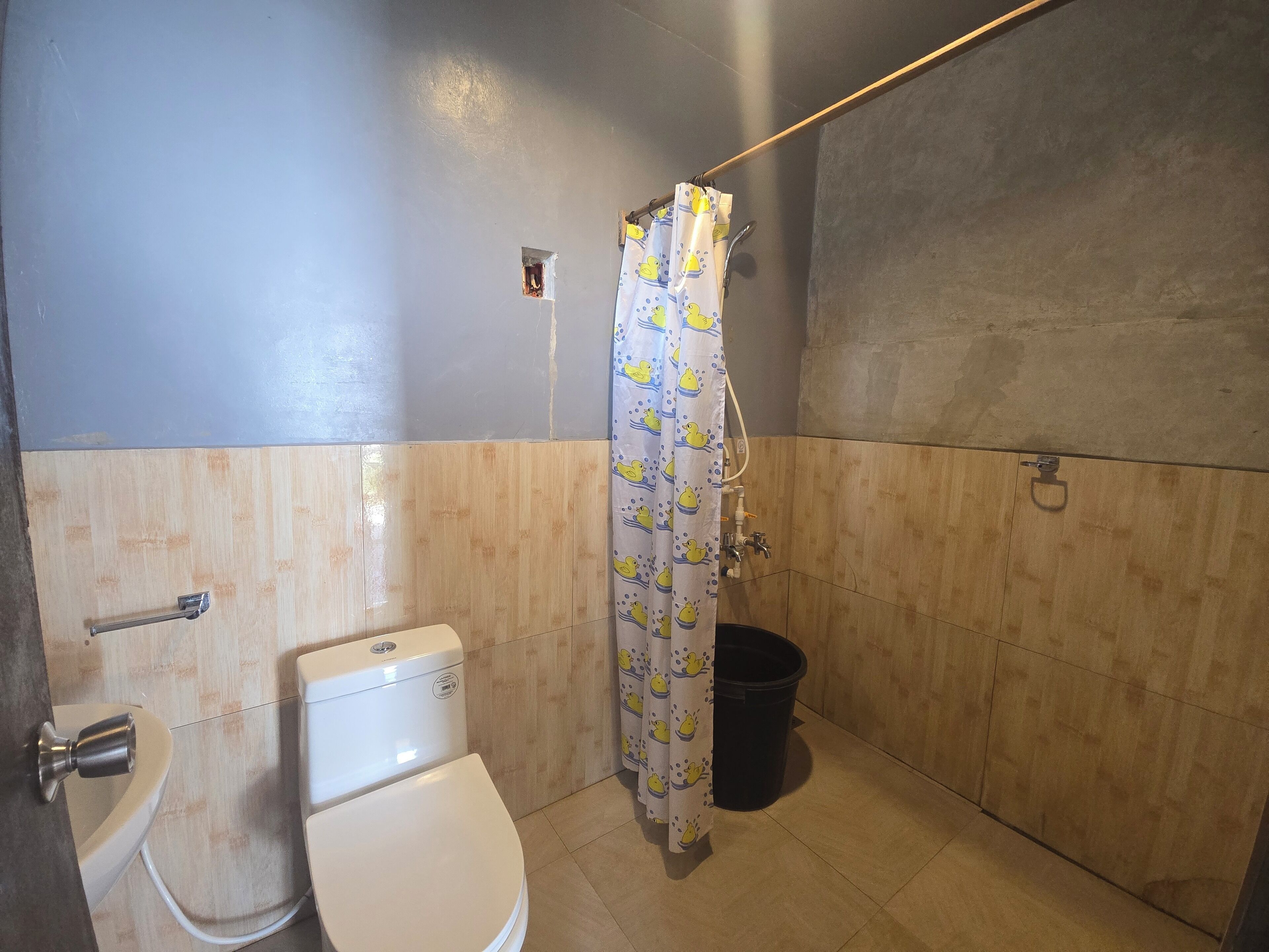 Un baño con inodoro, ducha con cortina y un cubo negro.