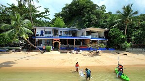 A beachfront property with a two-story building, a sandy beach, and palm trees. - Islandfront Cottages (El Nido)