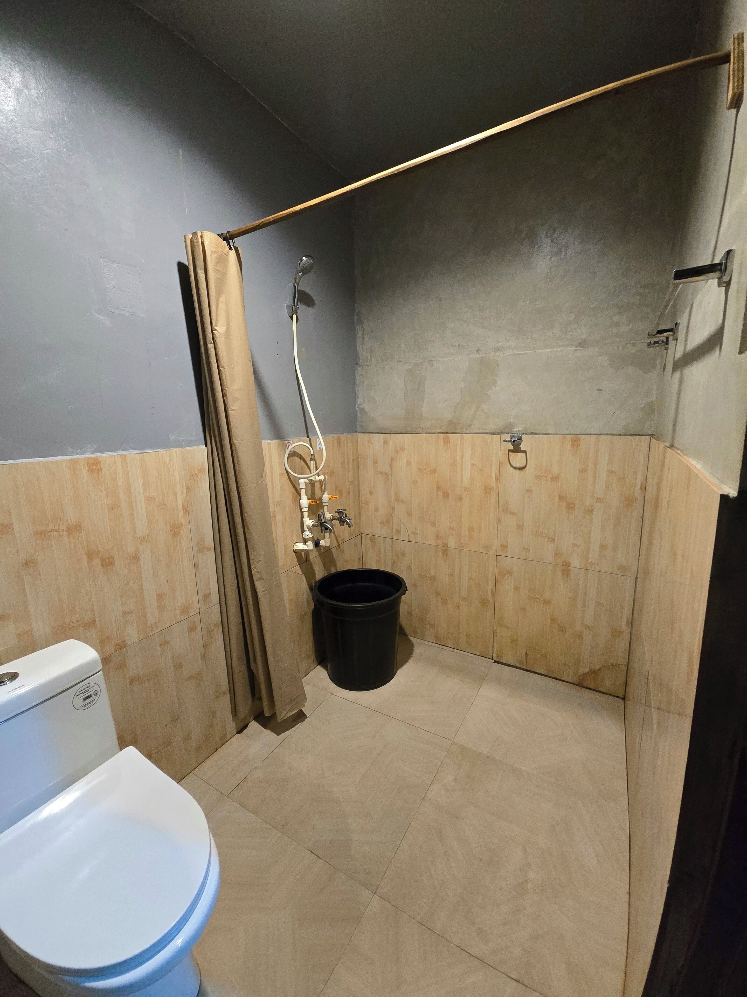 A small, compact bathroom with a toilet, shower, and a black bucket.