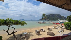 A beach with tables and chairs, boats, and a mountain in the background. - Islandfront Cottages (El Nido)