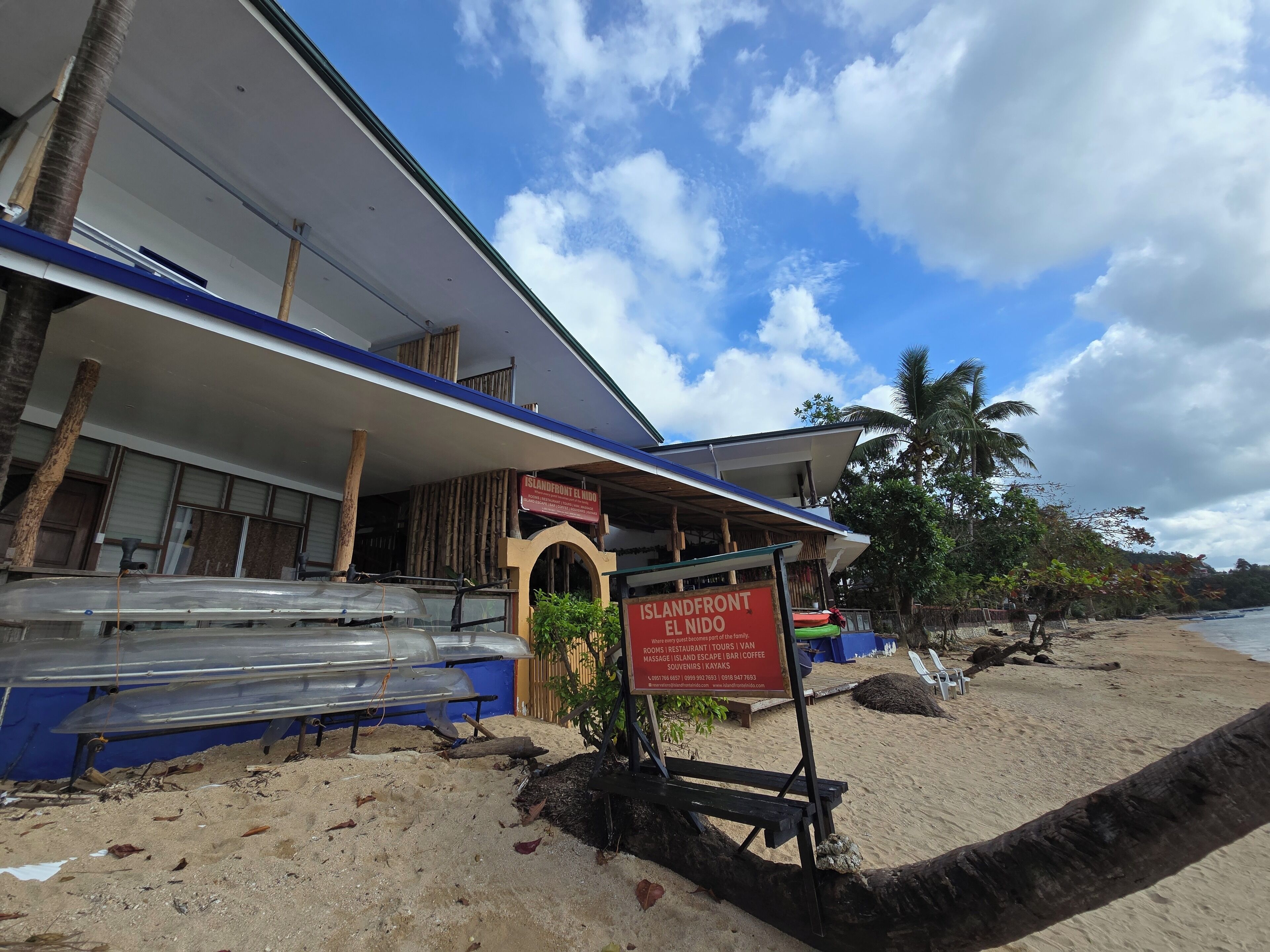 A beachside building with a sign for 'Islandfront El Nido' offering tours, restaurant, and souvenir shops.