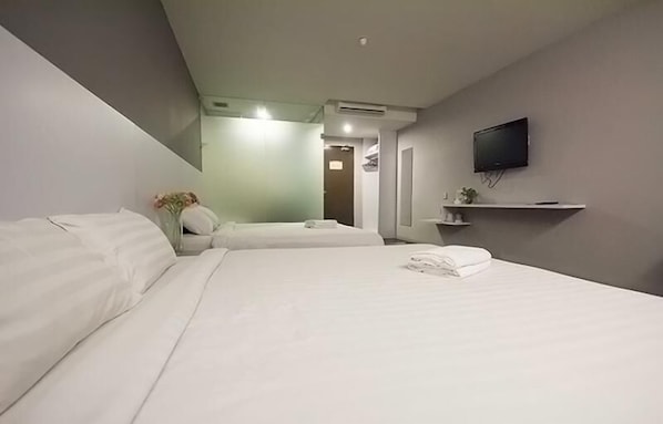 A hotel room with two beds, a flat-screen TV mounted on the wall, and a small shelf with a plant.