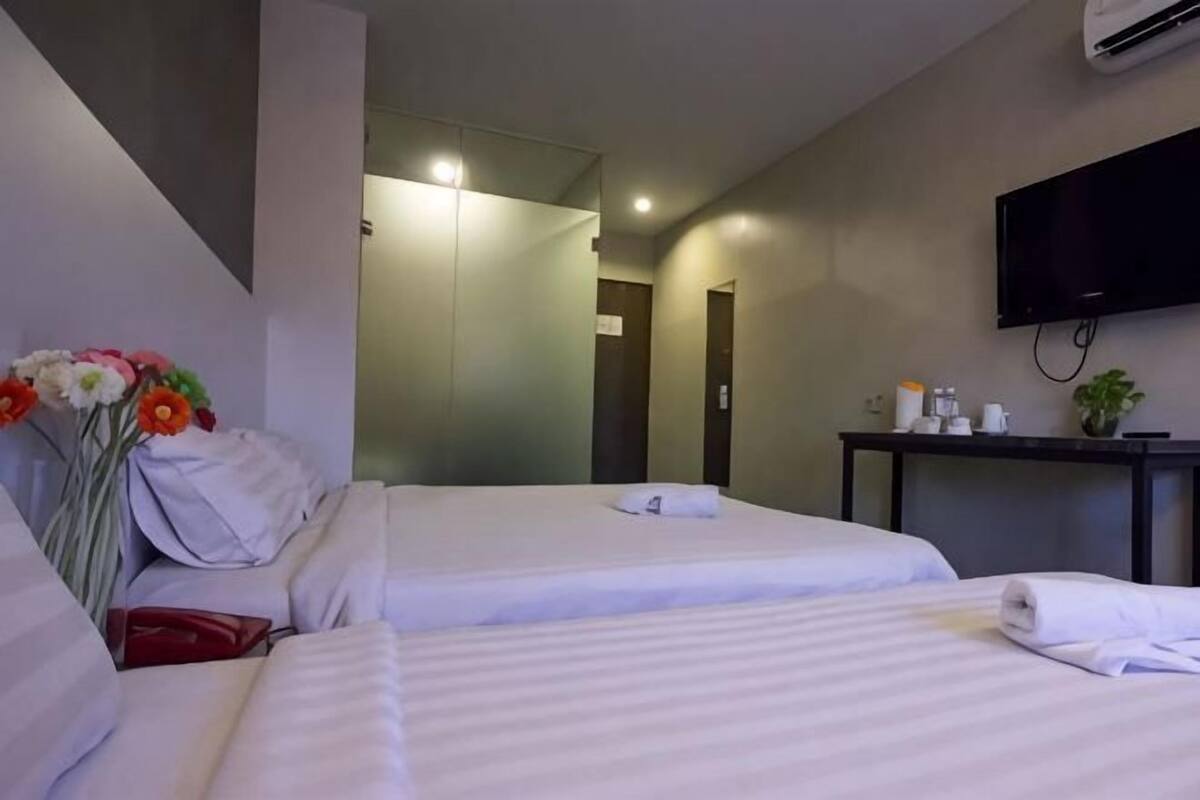 Una habitación de hotel con dos camas, televisión, escritorio con planta y espejo.