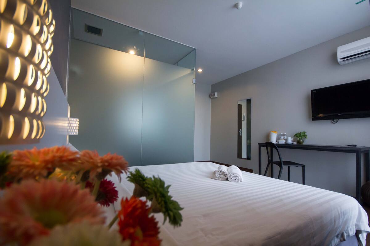 Una habitación de hotel moderna con una cama grande, un escritorio con silla, un televisor de pantalla plana y un espejo en la pared.