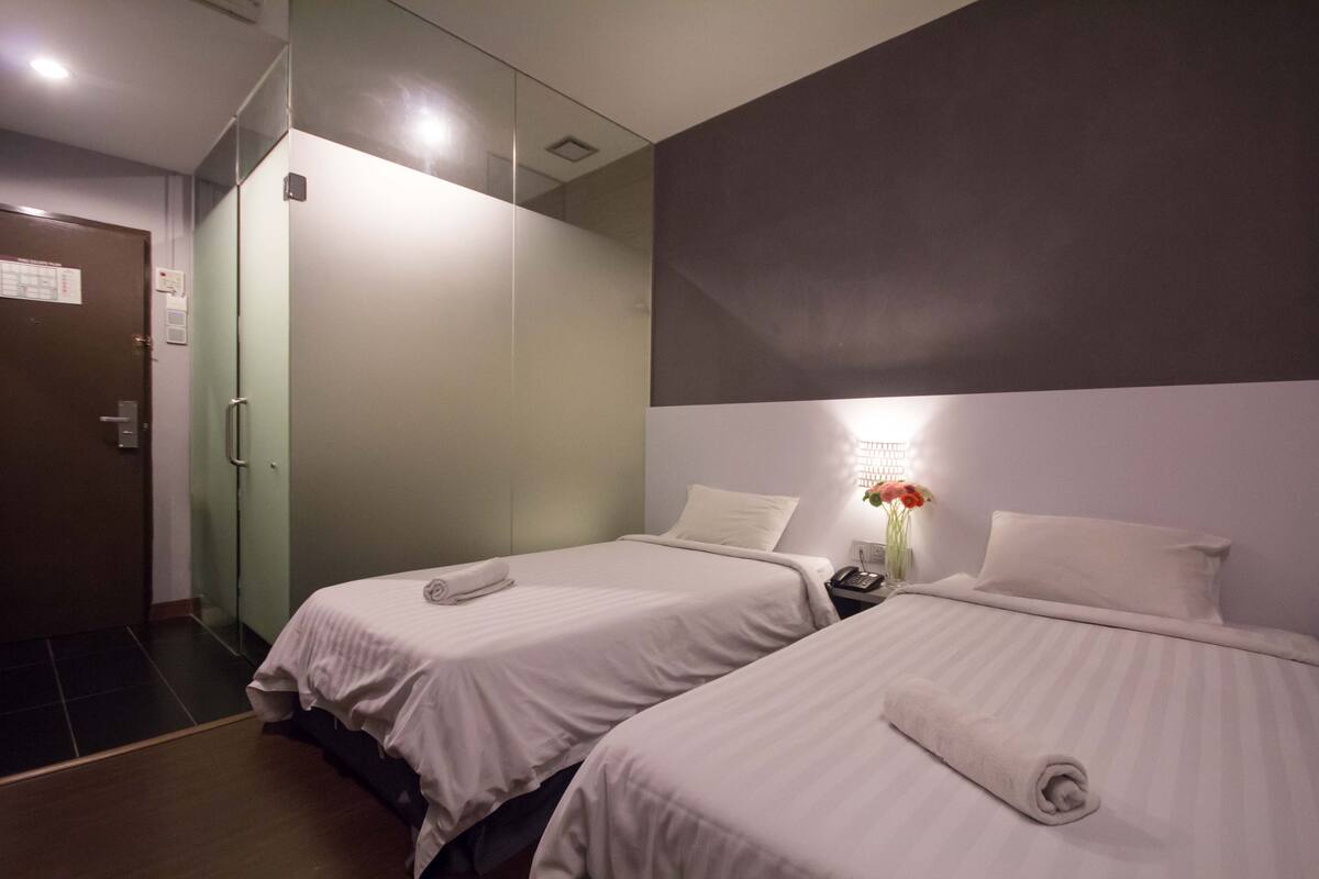 Habitación de hotel con dos camas, una mesita de noche, un teléfono en la pared y una puerta.