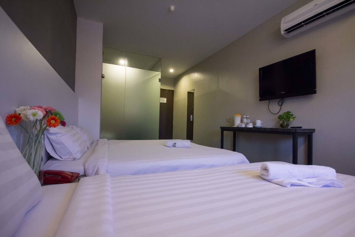 Habitación de hotel con dos camas, un televisor de pantalla plana, una mesita con artículos de aseo y un espejo.