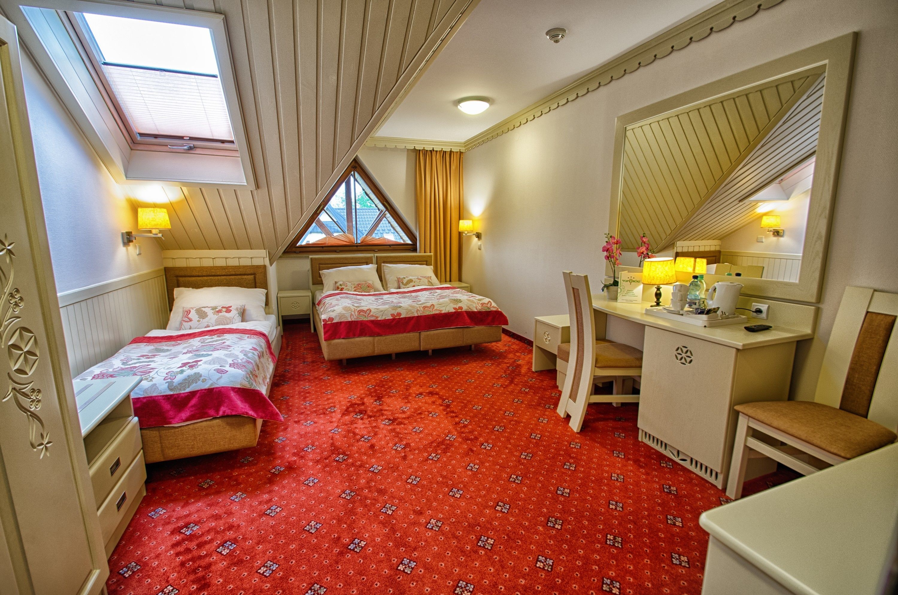 Habitación de hotel con dos camas, un escritorio, una silla, un espejo y una ventana con cortinas.