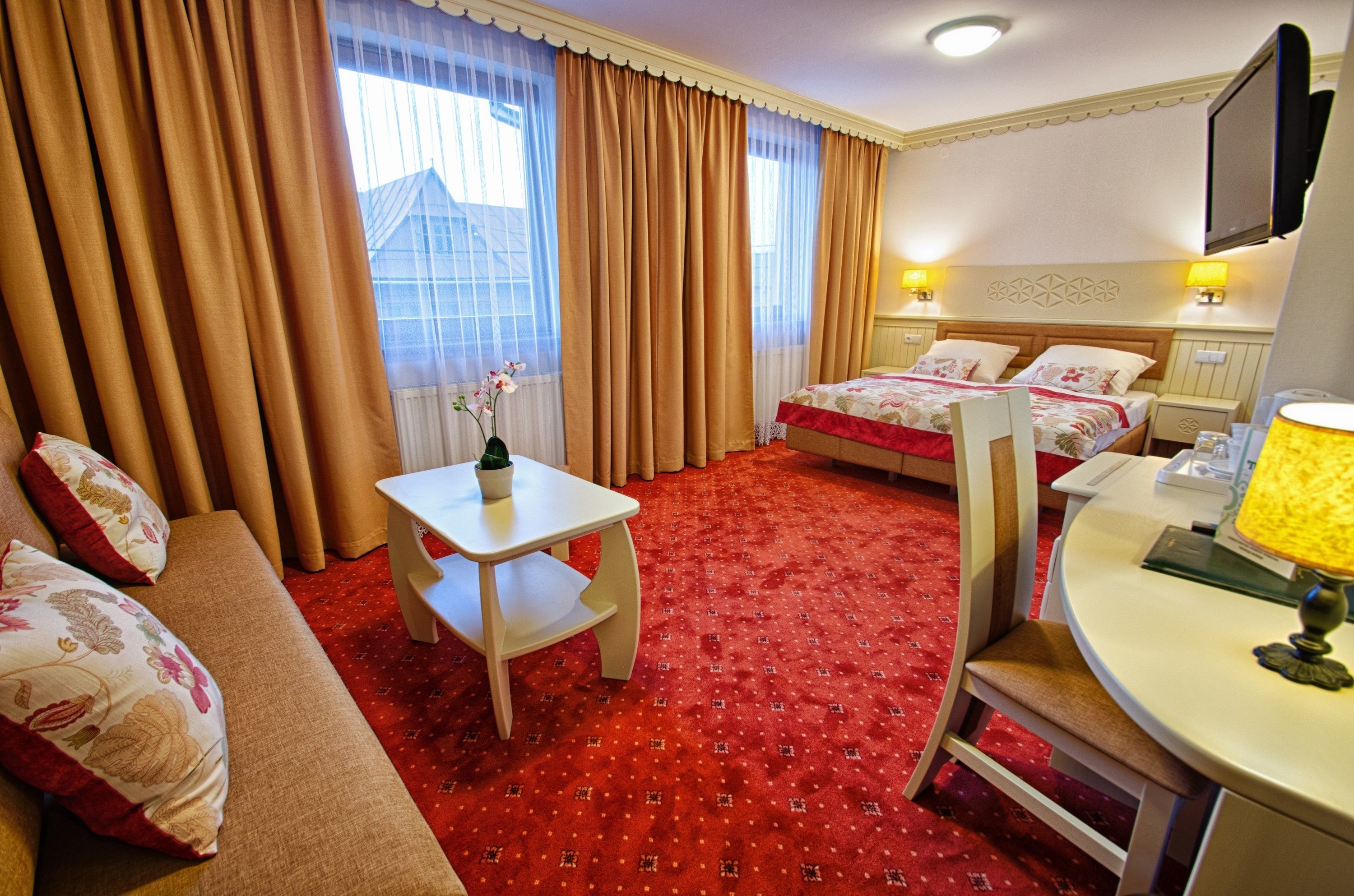 A hotel room with two beds, a sofa, a small table, and a TV.