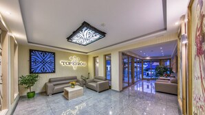 Un vestíbulo de hotel con una recepción, sofás, una mesa de centro y un ventanal con vistas al exterior.