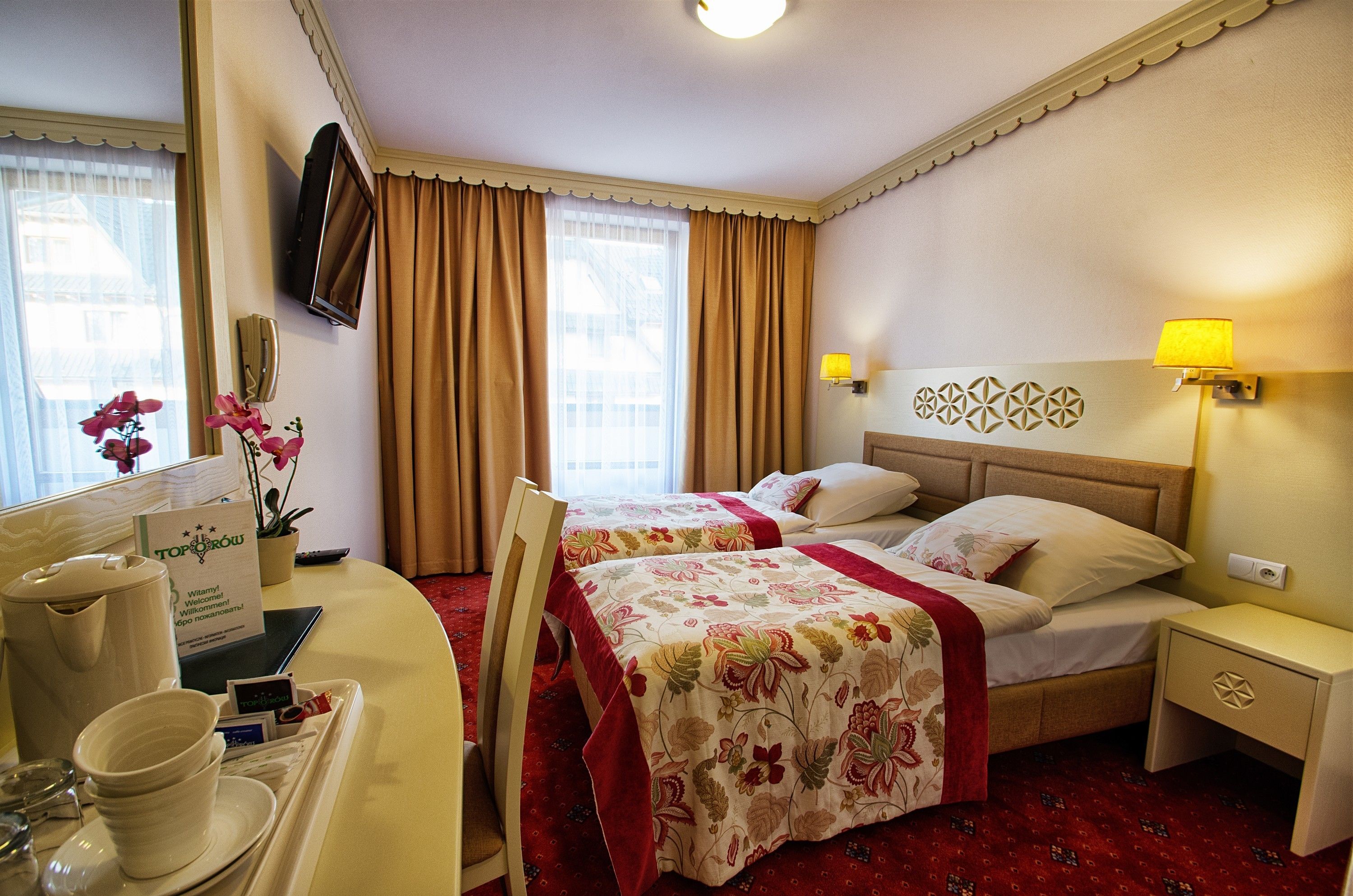 Habitación de hotel con dos camas, un escritorio con teléfono y cafetera, y un televisor montado en la pared.