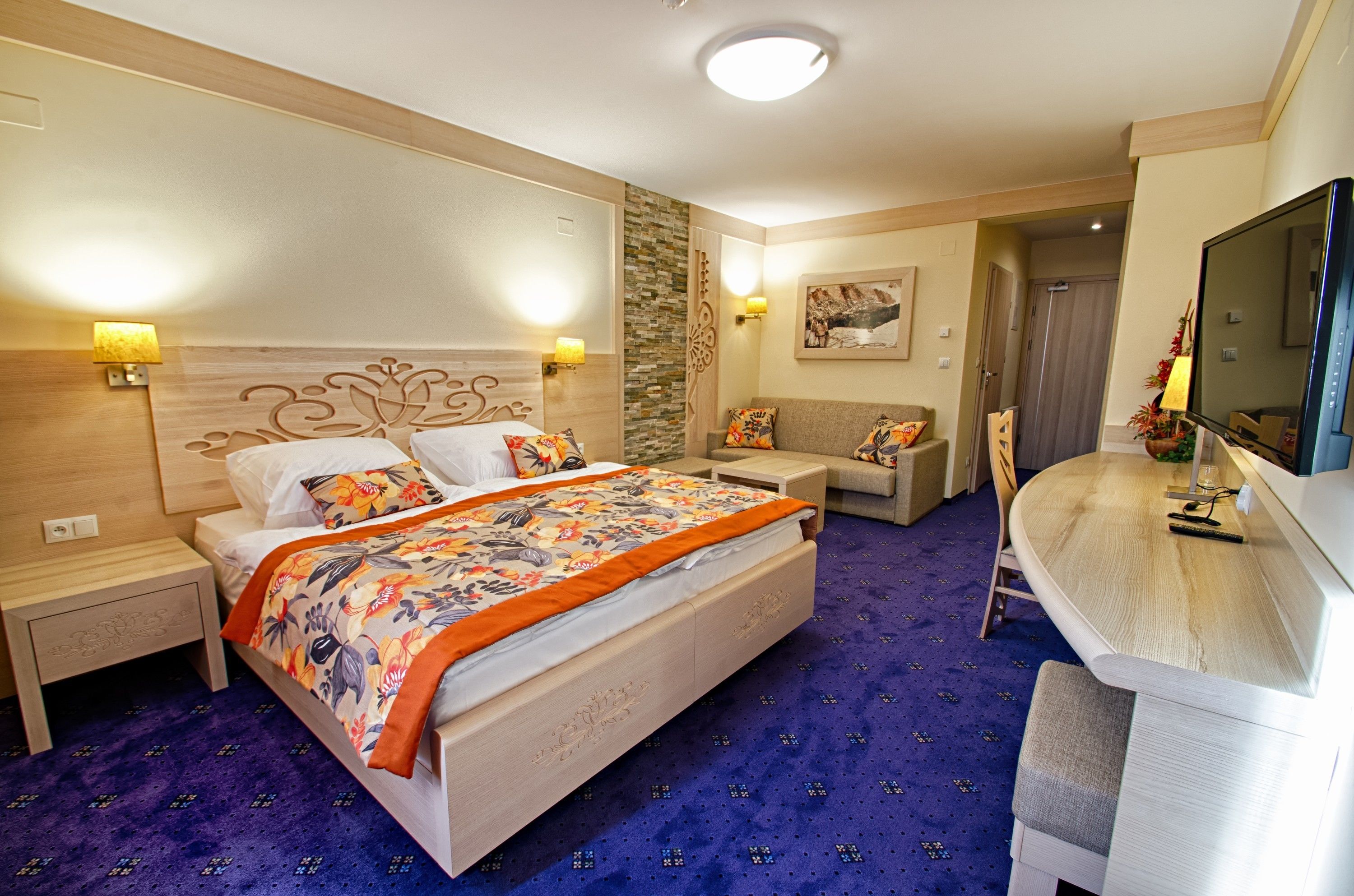 A bedroom with a large bed, a sofa, a TV, and a bathroom.
